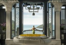 A woman standing in front of a large window with a view of the ocean